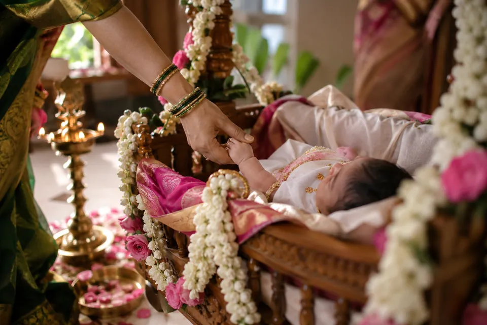 A baby in a jasmine-decorated cradle surrounded by brass lamps, in a warm family setting