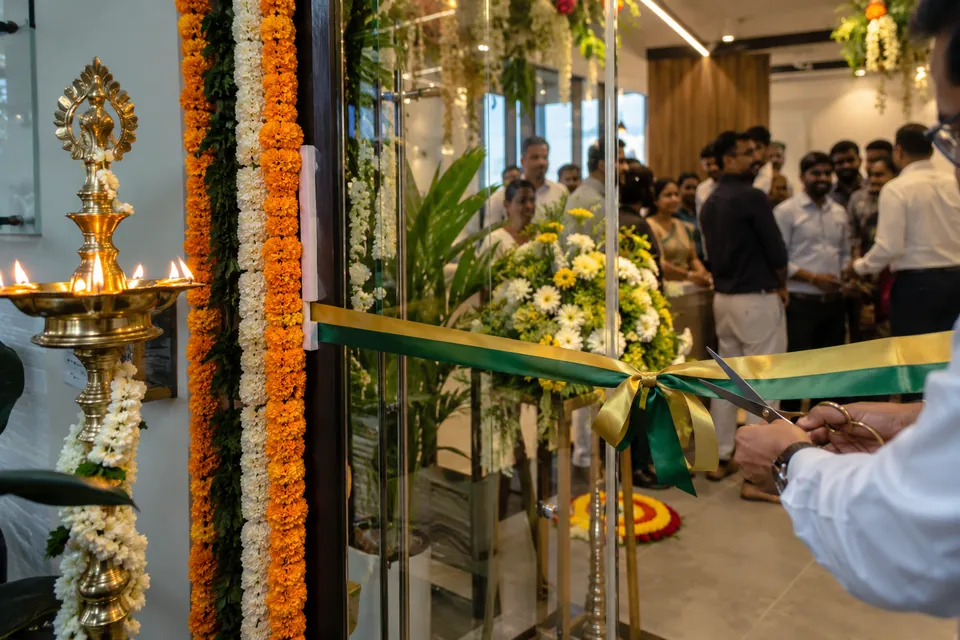 A ribbon being cut at an office inauguration beside a lit brass lamp and flower garlands